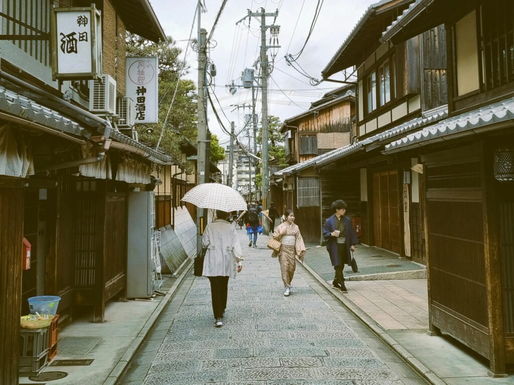 Authentic Kyoto street with people walking under umbrellas amidst traditional Japanese architecture.