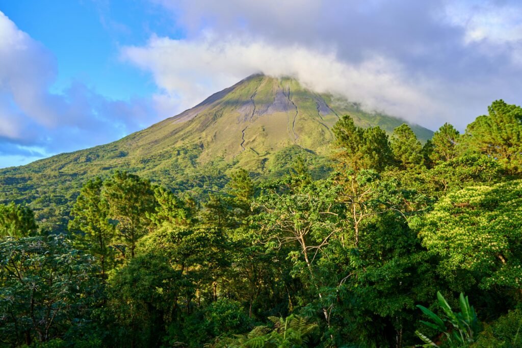 pexels-photo-29943339-29943339 Lush green forest with a prominent volcanic mountain under a blue sky with clouds.
