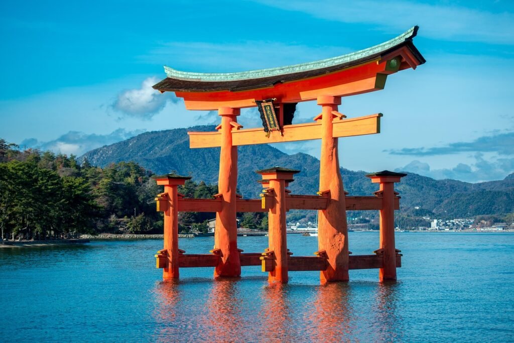 The iconic floating torii gate of Itsukushima Shrine in Hiroshima, Japan, standing above the blue waters of the bay. A UNESCO World Heritage landmark known for its traditional Shinto architecture, historic significance, and serene coastal landscape.