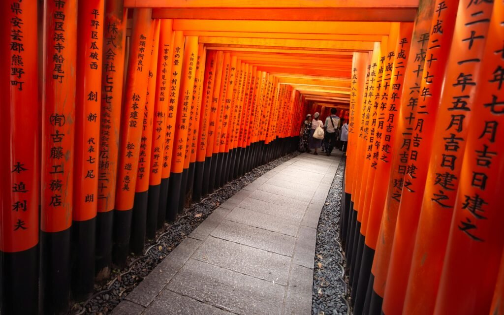 A vibrant path lined with orange torii gates at Fushimi Inari Shrine in Kyoto, Japan, attracting tourists.