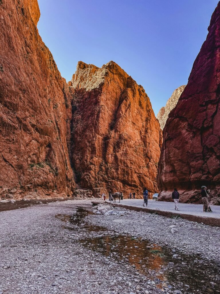 pexels-photo-33530297-33530297 Sunlit red rock walls of Todra Gorge with people exploring the scenic path.