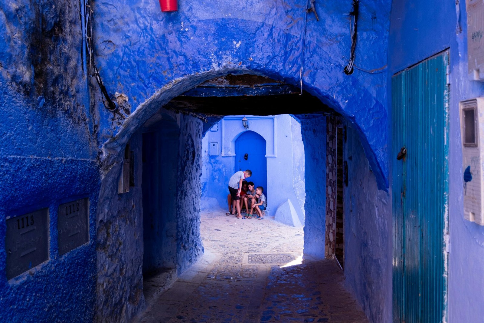 Kids enjoy a playful moment in Chefchaouen's iconic blue alleyway. Colorful and lively scene.