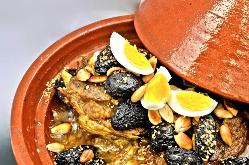 Close-up of Moroccan lamb tagine with prunes, almonds, and boiled eggs in a clay pot.