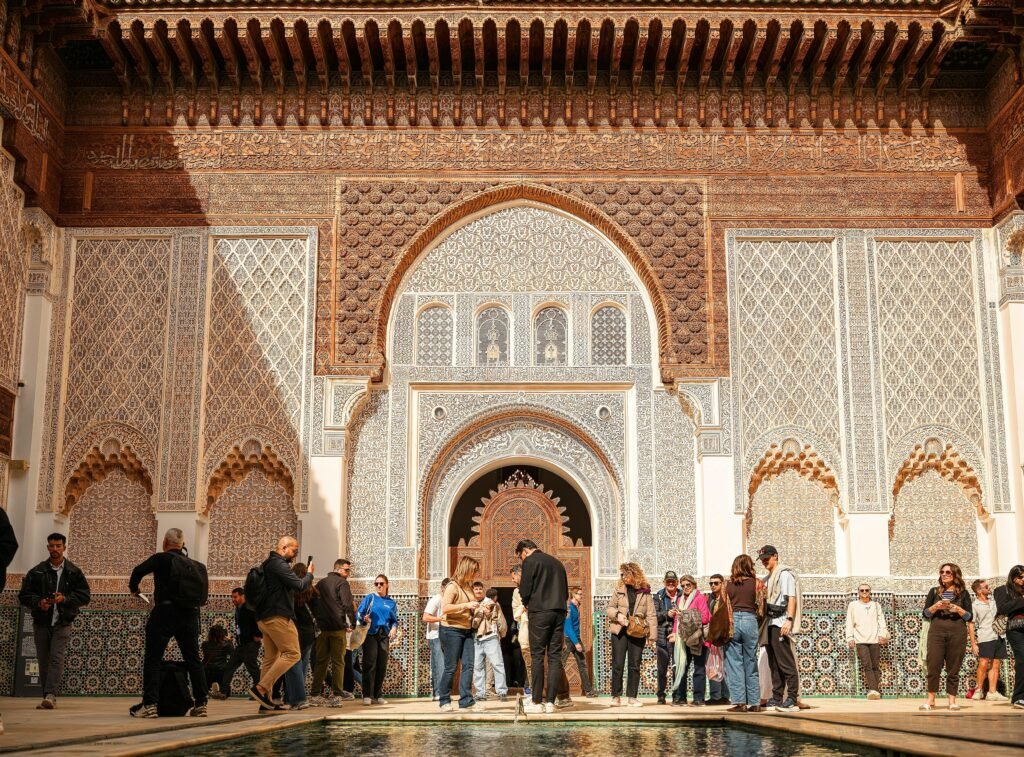 Group of tourists exploring Ben Youssef Madrasa's intricate architecture in sunny Marrakech.