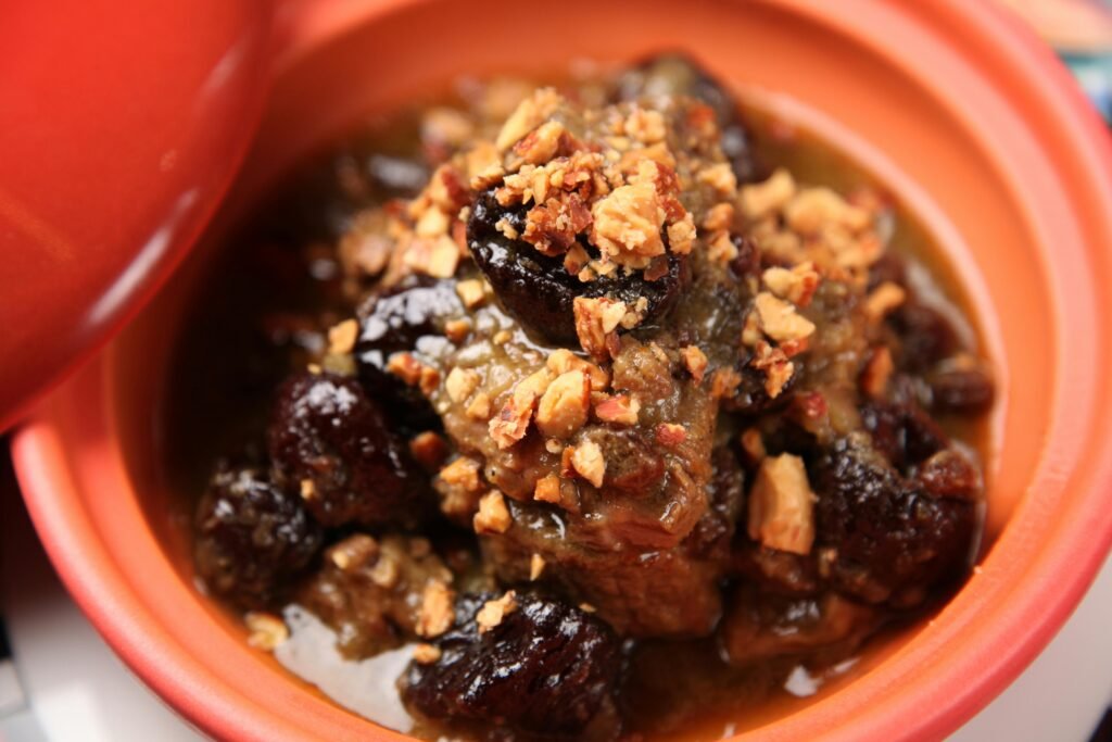 Close-up of a delicious beef stew garnished with nuts, served in an orange ceramic bowl.