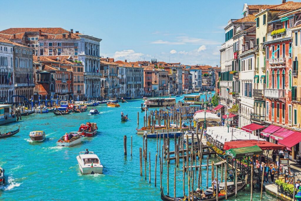Explore the bustling Grand Canal in Venice with boats, gondolas, and stunning architecture under a bright summer sky.