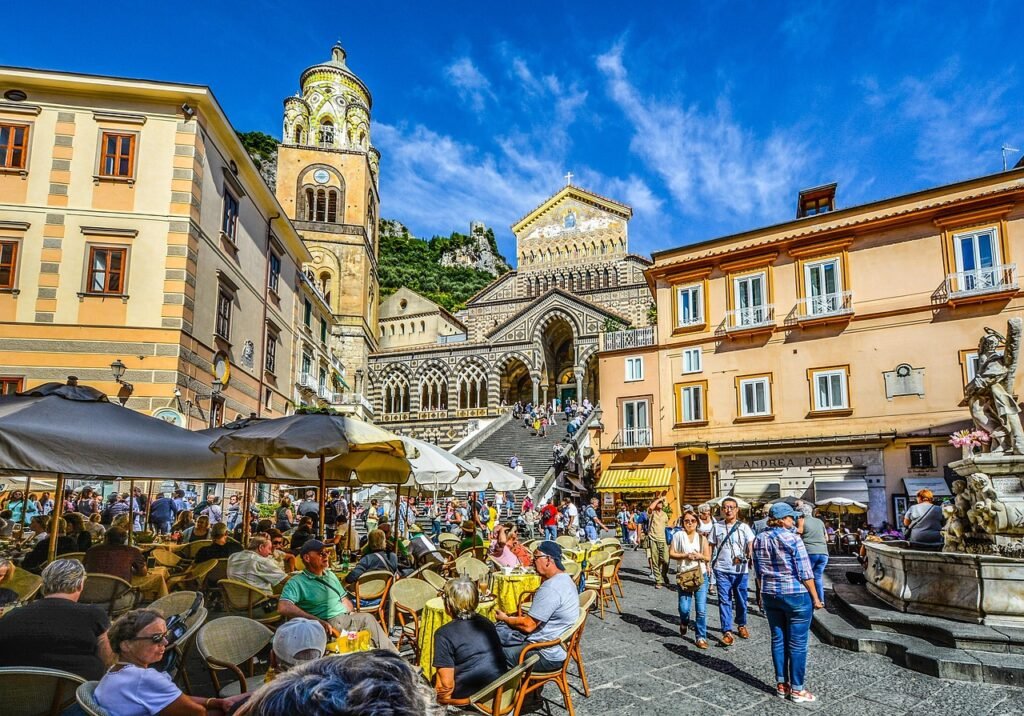 Piazza Duomo in Amalfi, Italy, with tourists, cafés, umbrellas, and Amalfi Cathedral