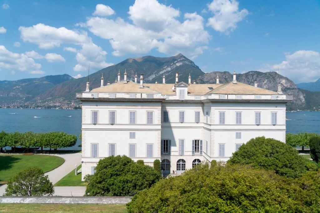 A grand villa surrounded by lush gardens and mountains near the Italian lake.