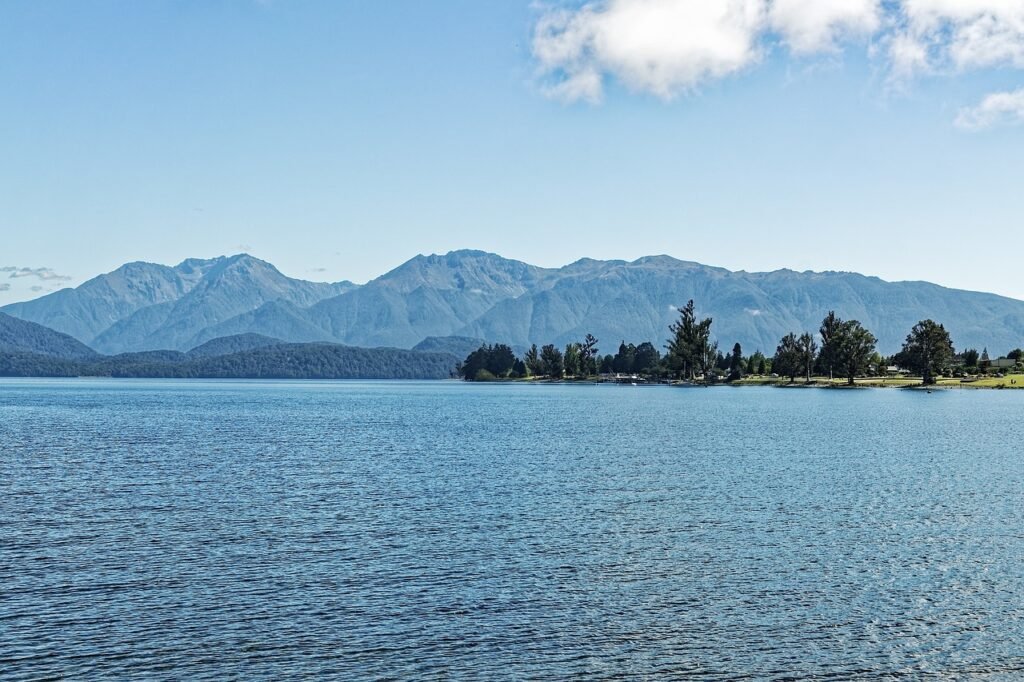Scenic view of Lake Te Anau in Fiordland National Park, New Zealand, with blue water, mountains, and clouds across the landscape.