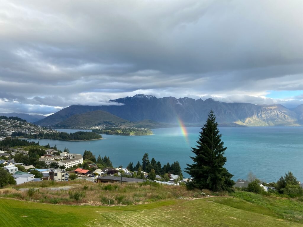 Aerial view of Queenstown, New Zealand with Lake Wakatipu, mountains, and a rainbow.