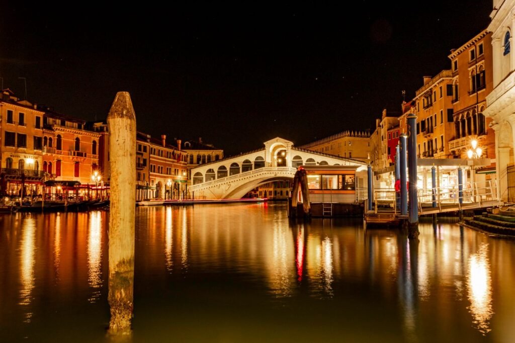 Stunning night view of the illuminated Rialto Bridge in Venice, Italy, reflecting on the canal.