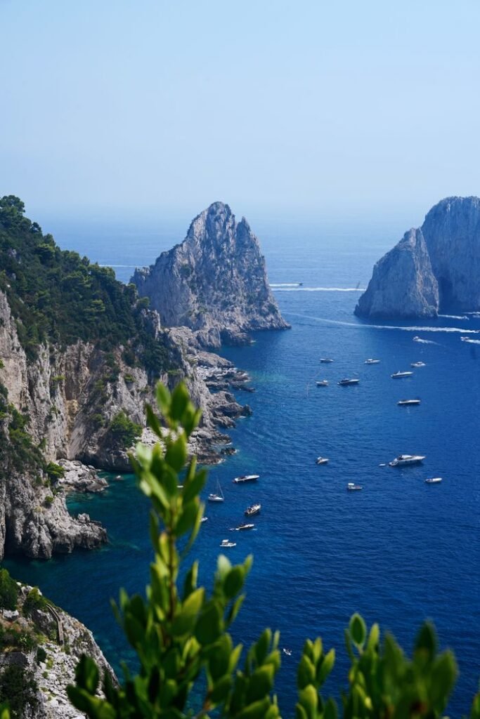 Majestic view of Capri's coastline and iconic rock formations with boats on the clear blue sea.