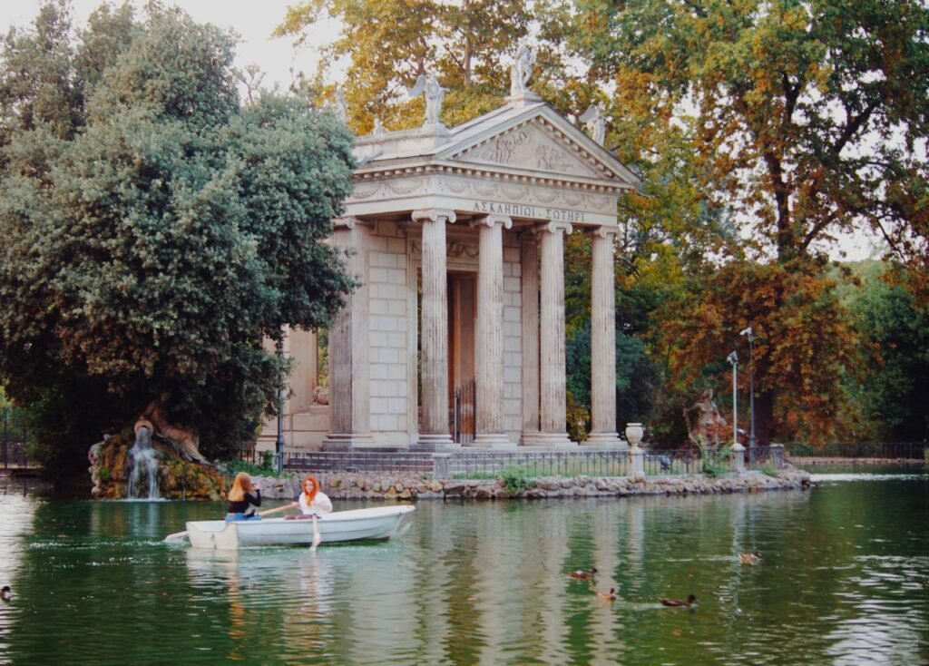 A serene canal scene with a boat navigating by an ancient temple in Rome's Villa Borghese.