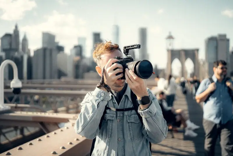 A photographer takes a picture on the iconic Brooklyn Bridge during a 4 day New York itinerary, with the New York City skyline in the background.